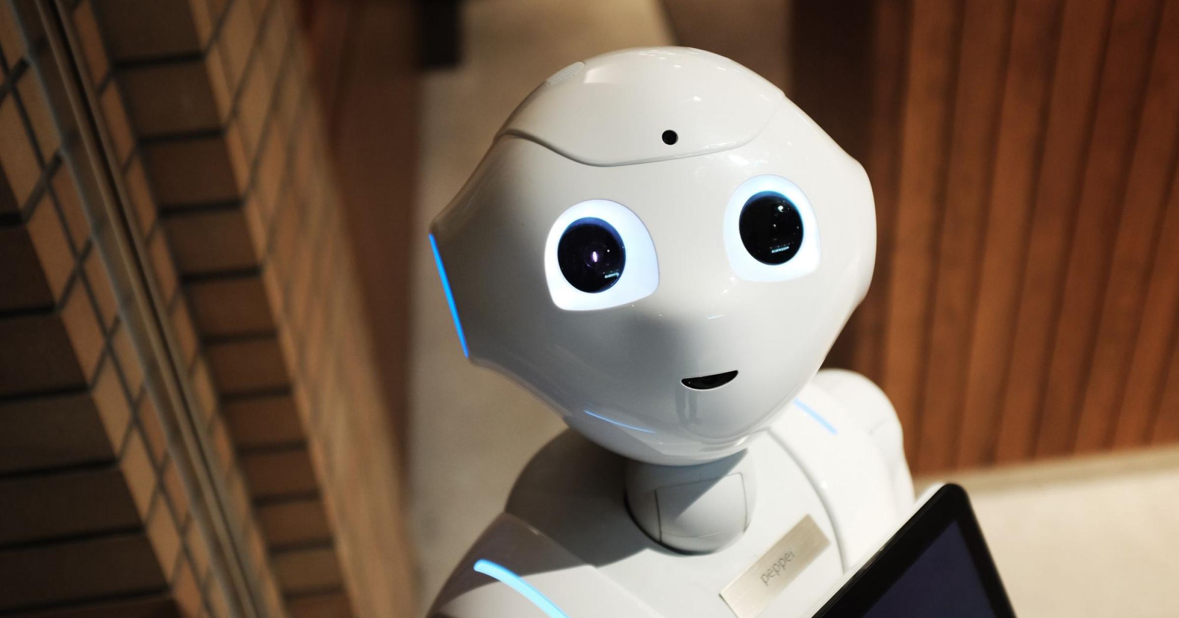 A white robot with glowing eyes and simple smile looks up at the camera.